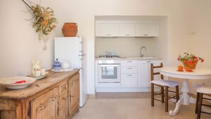 Une cuisine compacte avec des meubles blancs, un plan de travail en bois et un coin repas comprenant une table et des chaises blanches.