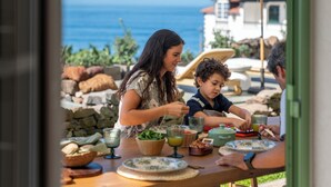 A dining table with food and drinks, a view of the ocean, and a stone wall in the background.