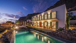 A modern hotel with a pool, outdoor seating, and a mountain backdrop.