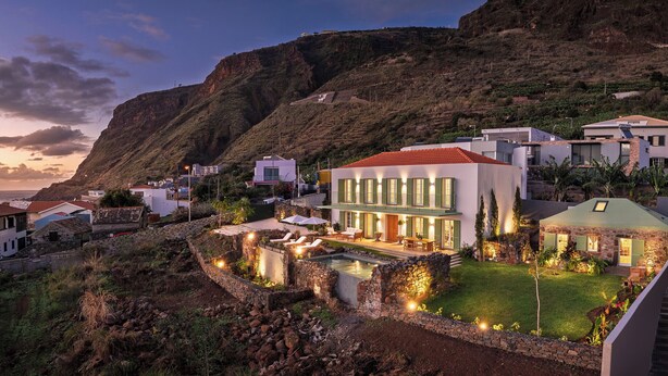 A coastal property with a pool, stone walls, and a view of the sea.