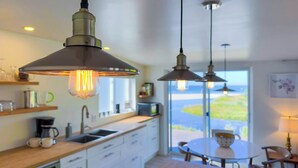Une cuisine moderne avec des luminaires suspendus, une machine à café et une vue sur la mer.