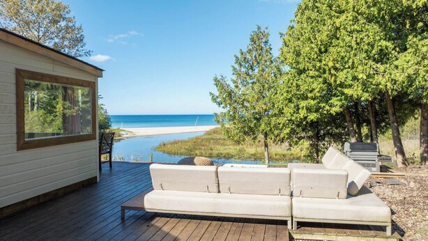 Une terrasse avec un canapé blanc et une table, donnant sur une plage et une étendue d’eau.