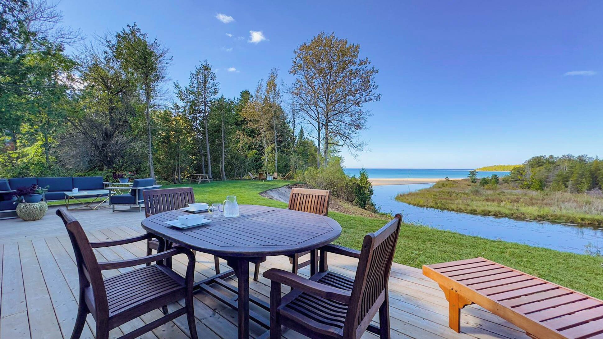 An outdoor deck with a round table and chairs, overlooking a body of water and a forested area.