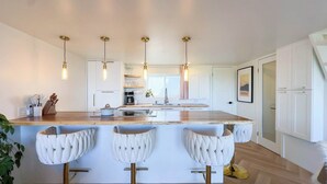 A modern kitchen with a central island, bar stools, pendant lighting, and white cabinetry. - Modern Classic, Lake Views (Kincardine)