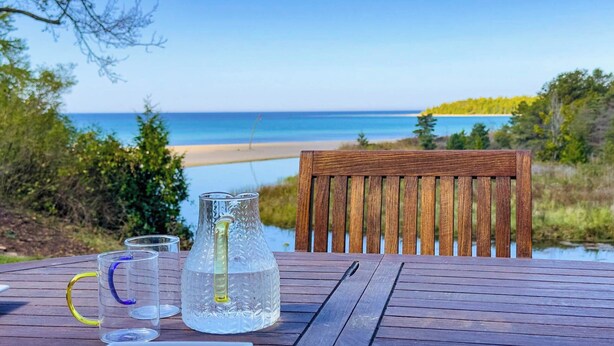A wooden table with a glass pitcher and two glasses, overlooking a beach and water. - Modern Classic, Lake Views (Kincardine)