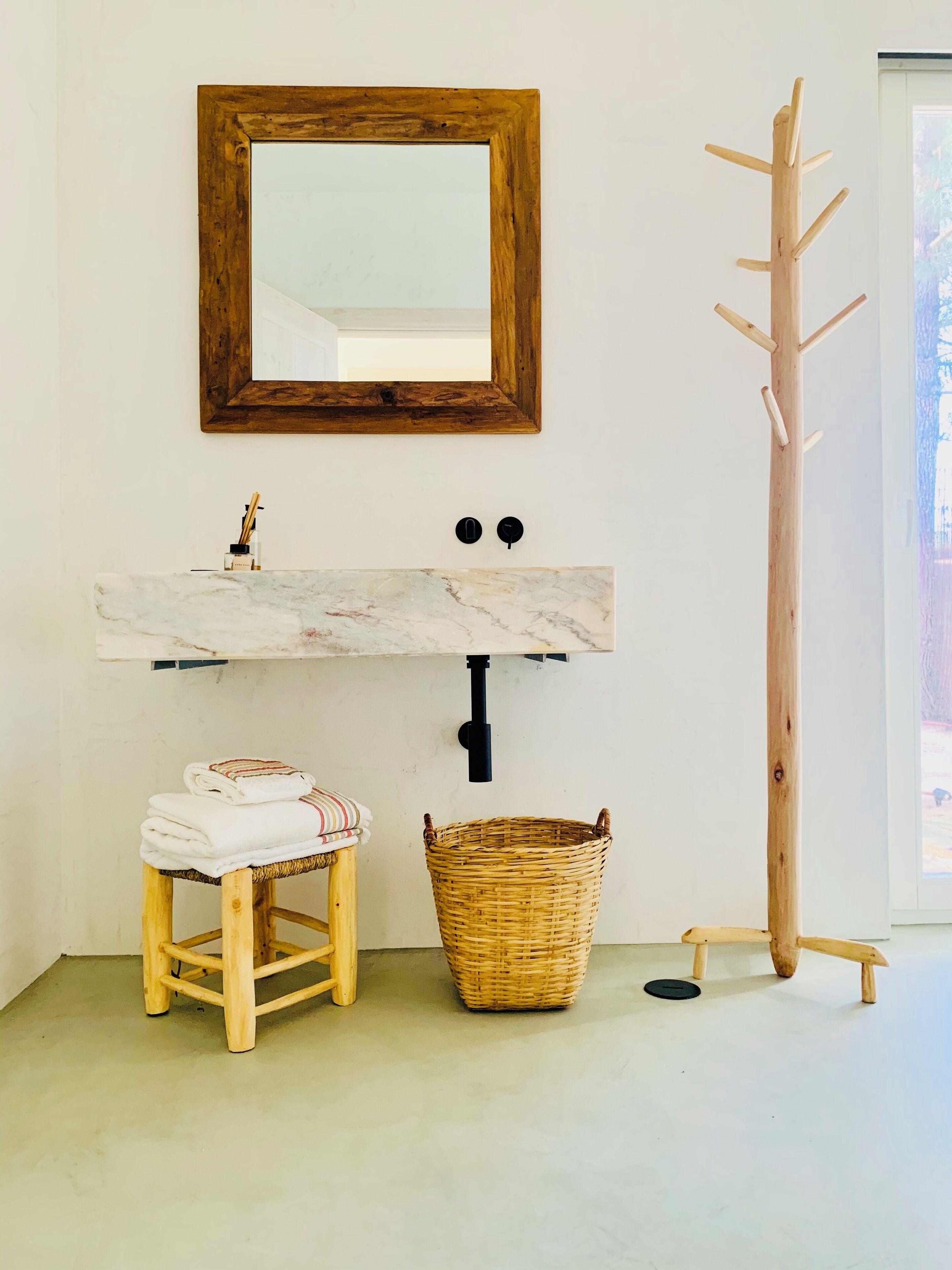 Un bagno con uno sgabello di legno, un lavabo in marmo, un cesto di vimini e un appendiabiti in legno.