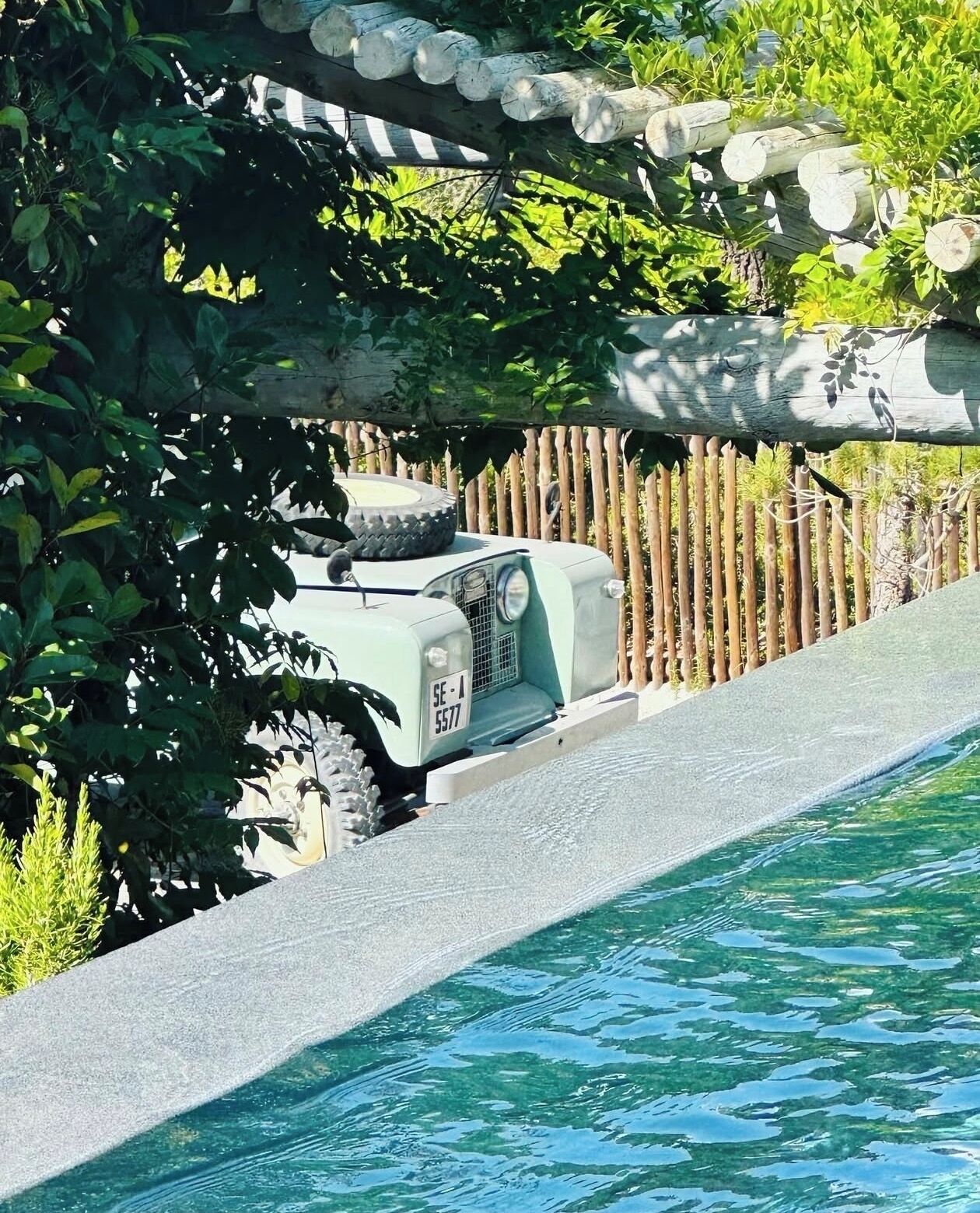 A pool with a wooden fence and a vehicle partially visible behind it.