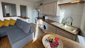 A compact living space with a grey sofa, a wooden dining table, a washing machine, a microwave, and a sink with a modern faucet. - Apartment in Gentilly, 2 steps from Paris (Gentilly)
