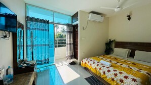 A hotel room with a bed, a ceiling fan, an air conditioning unit, a window with curtains, and a view of palm trees outside. - Hotel Nice Look Kuakata (Kalapara)