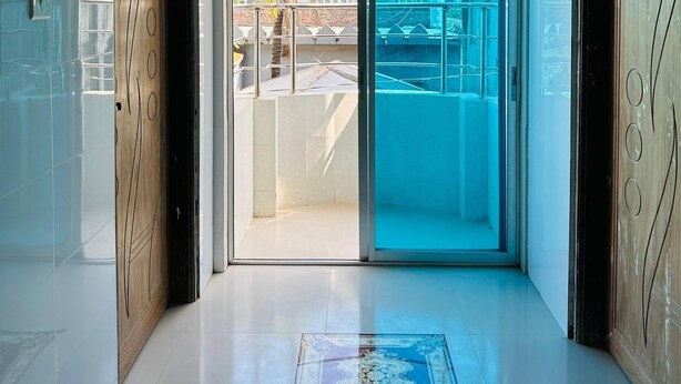 A hallway with a glass door leading to an outdoor area, a ceiling-mounted security camera, and a tiled floor. - Hotel Nice Look Kuakata (Kalapara)