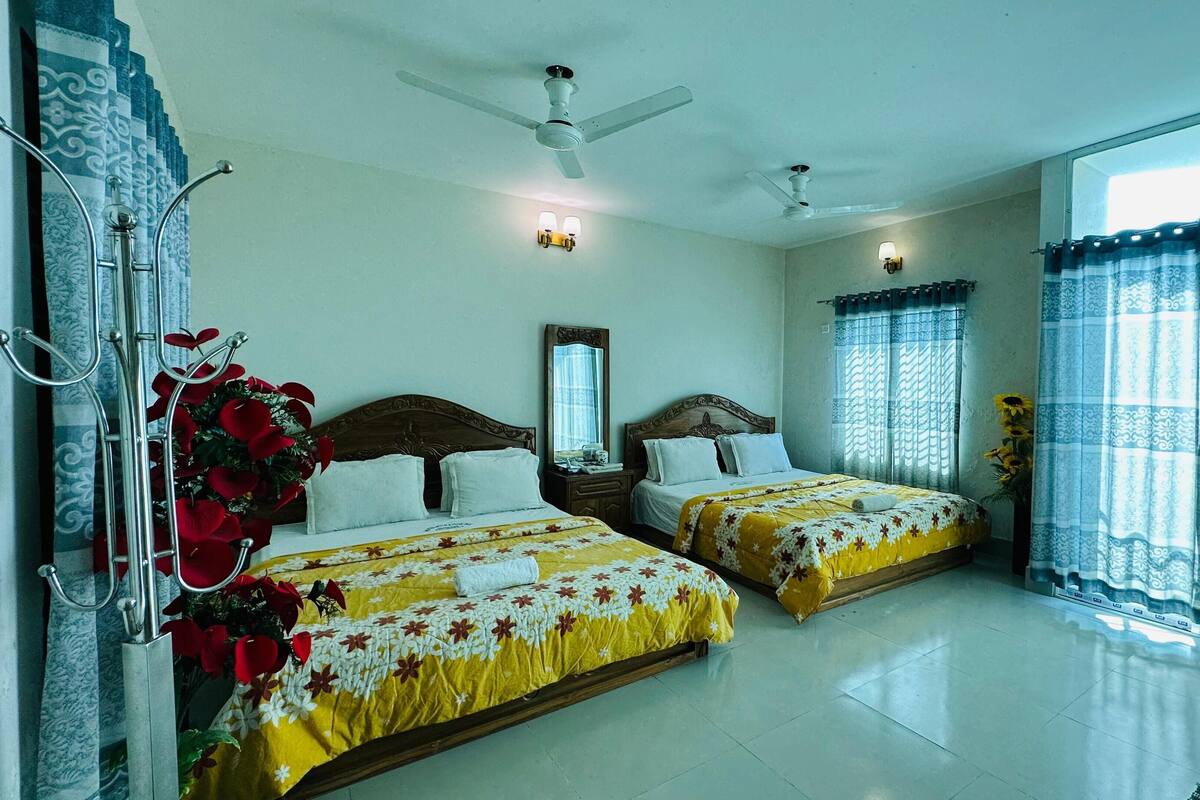 A hotel room with two beds, a ceiling fan, a large window with curtains, and a decorative mirror.