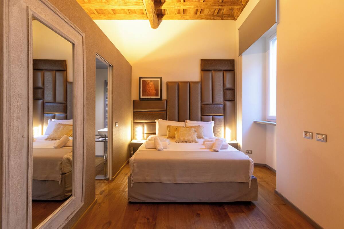 A bedroom with a large bed, a mirror, a bedside table, and a headboard.