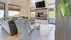 A modern living room with a fireplace, grey sofas, and a large window offering a view. - Dreamy Hilltop View: Roseburg Wine Country Retreat (Roseburg)