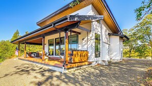 A modern house with a covered porch, large windows, and a flag. - Dreamy Hilltop View: Roseburg Wine Country Retreat (Roseburg)