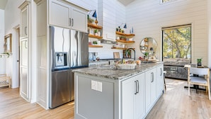 A modern kitchen with white cabinetry, a stainless steel refrigerator, and wooden shelves with plants. - Dreamy Hilltop View: Roseburg Wine Country Retreat (Roseburg)
