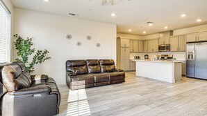 Una cocina moderna con una isla central, un área de comedor con un sofá de cuero y un ventilador de techo.
