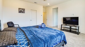 Un dormitorio con una cama, una silla, un televisor y un ventilador de techo.
