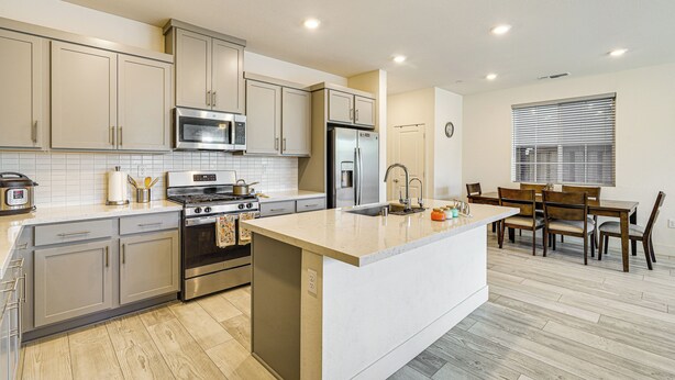 Una cocina moderna con electrodomésticos de acero inoxidable, una isla central con pileta y un comedor con sillas y mesa de madera.