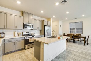 Una cocina moderna con electrodomésticos de acero inoxidable, una isla central con pileta y un comedor con sillas y mesa de madera.