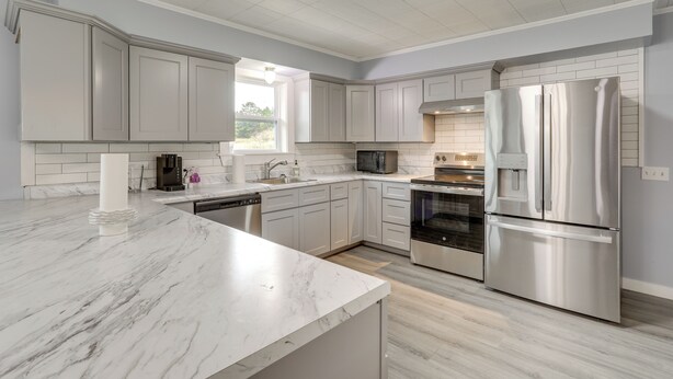 A modern kitchen with white cabinetry, a marble countertop, stainless steel appliances, and a light wood floor. - Hike, Fish & Boat: Secluded Mountain View Home (Mountain View)