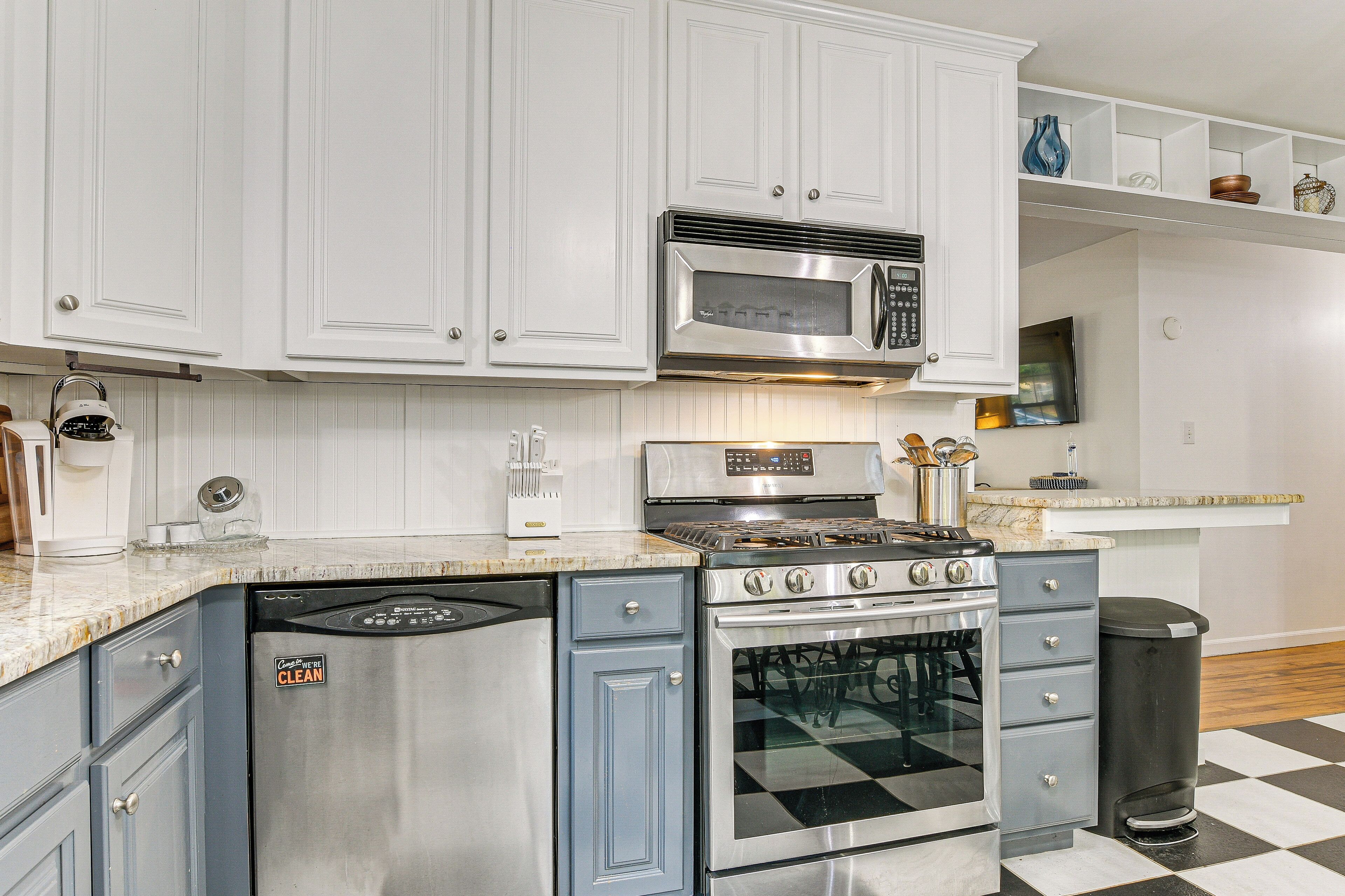 Una cocina con gabinetes blancos, estufa de acero inoxidable, microondas y lavavajillas.