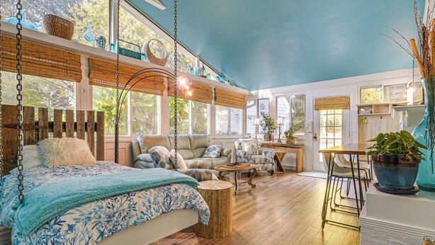 A spacious room with a large bed, a sofa, and a dining area. There are multiple windows providing natural light and views of the outdoors. - 4 Mi to Falls Lake: Dog-friendly Wake Forest Home (Wake Forest)