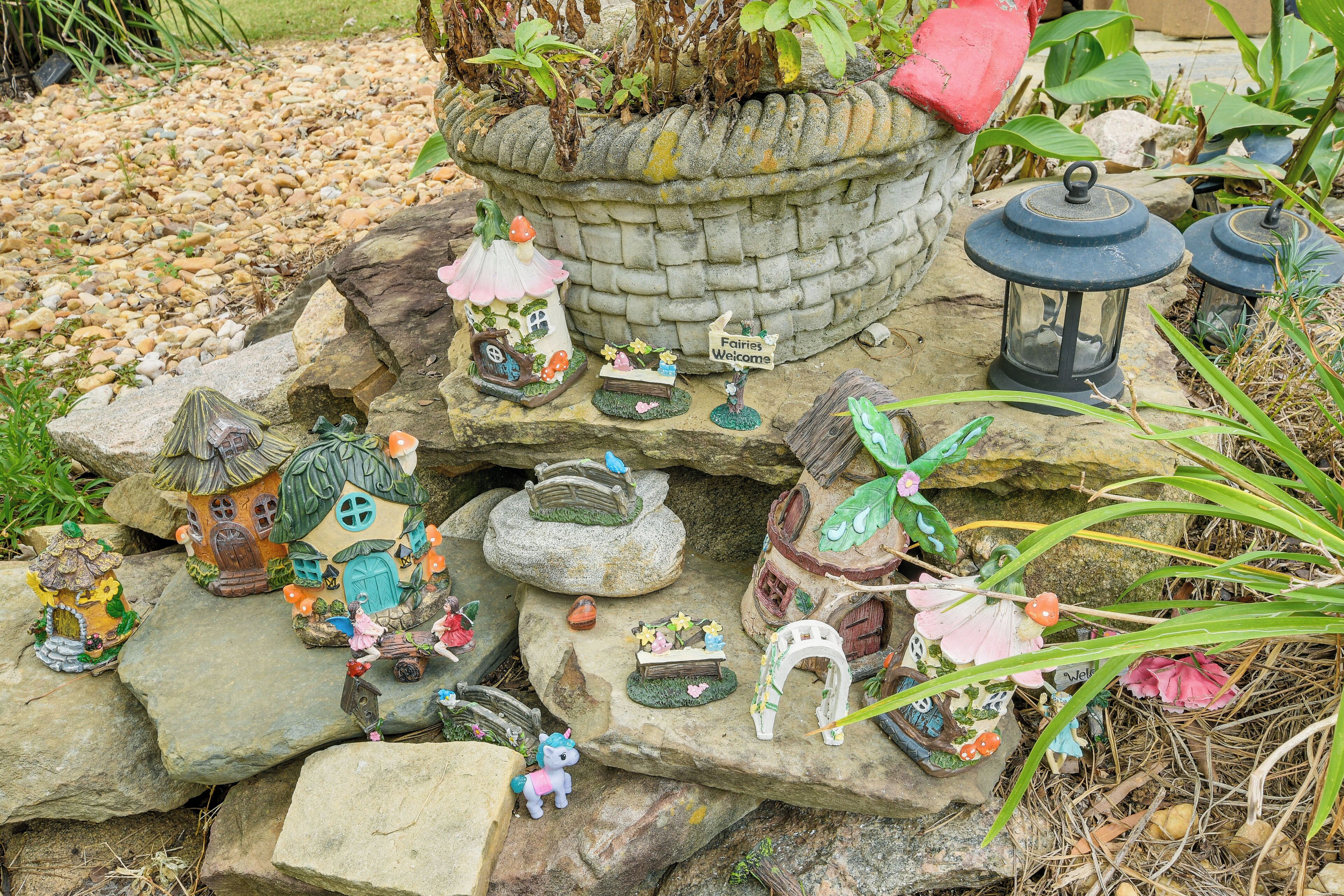 Un jardin agrémenté de diverses décorations sur le thème des fées, notamment une maison, des lanternes et un panneau sur lequel on peut lire : « Les fées sont les bienvenues ».