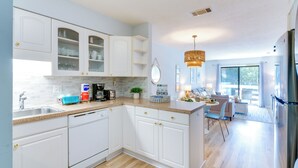 A modern kitchen with white cabinets, a granite countertop, and a dining area with a view. - Walk to Beach: Condo w/ Balcony in Hilton Head! (Hilton Head Island)