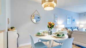 A dining area with a round table, blue chairs, and a hanging light fixture. - Walk to Beach: Condo w/ Balcony in Hilton Head! (Hilton Head Island)