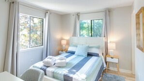 A bedroom with a bed, two bedside tables, and a window. - Walk to Beach: Condo w/ Balcony in Hilton Head! (Hilton Head Island)
