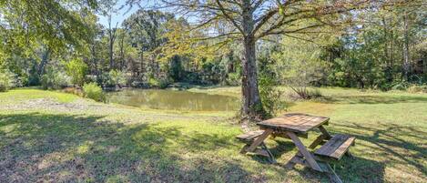 A picnic table in a grassy area with a pond and trees in the background.