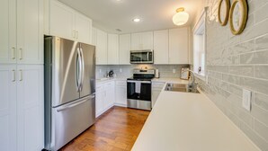 A modern kitchen with white cabinets, stainless steel appliances, and a wooden floor. - Fire Pit & Grill: Tyler Home on 5 Acres! (Tyler)