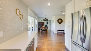 A modern kitchen with white cabinets, a stainless steel refrigerator, and a wooden herringbone floor. - Fire Pit & Grill: Tyler Home on 5 Acres! (Tyler)