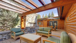 A log cabin with a stone fireplace, outdoor seating area, and a view of the surrounding forest. - Sun Valley Log Home w/ Hot Tub & Mtn Views! (Sun Valley)