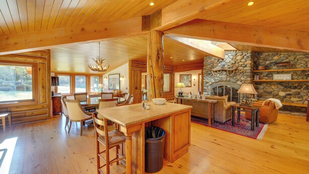 A spacious wooden interior with a stone fireplace, wooden dining area, and large windows. - Sun Valley Log Home w/ Hot Tub & Mtn Views! (Sun Valley)