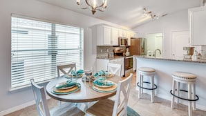 A modern kitchen with white cabinets, a central island, and a dining area with a round table and chairs. - On-site Canal Access: Luxe Home in Palm Coast! (Palm Coast)