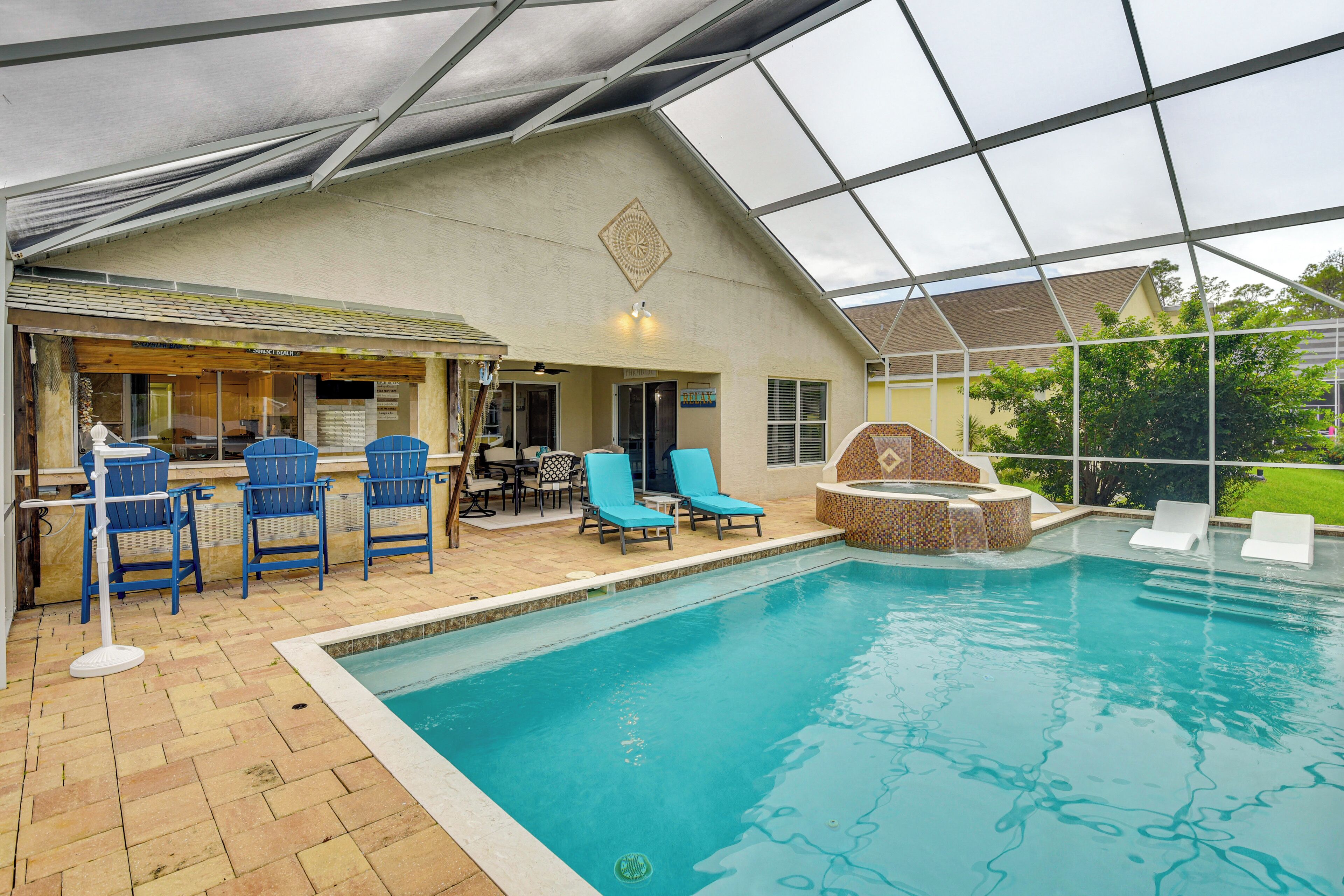 An indoor swimming pool with blue chairs and a sunken seating area, surrounded by a covered patio with a bar and seating.