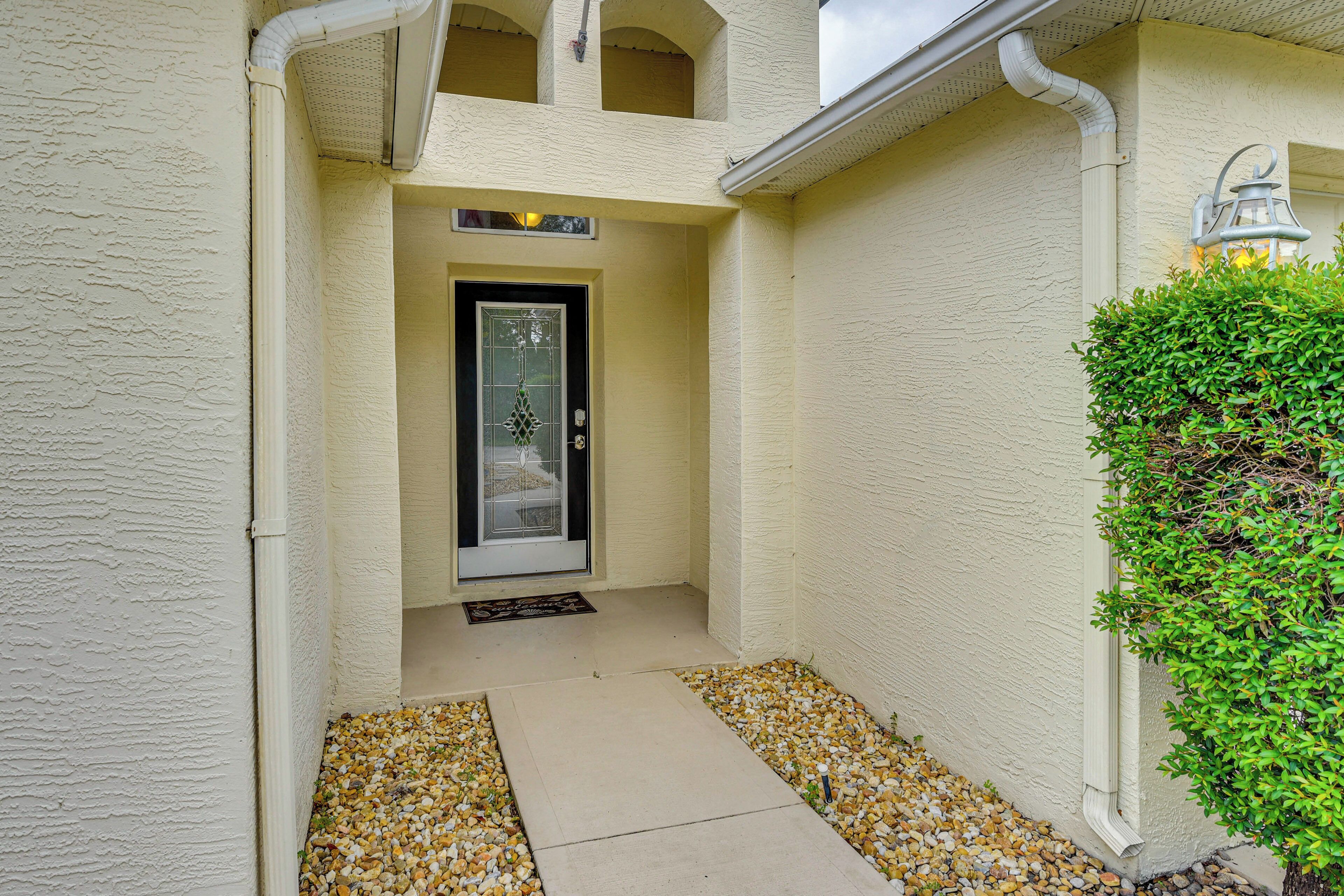 A house entrance with a door, a small porch area with gravel, and a green hedge.