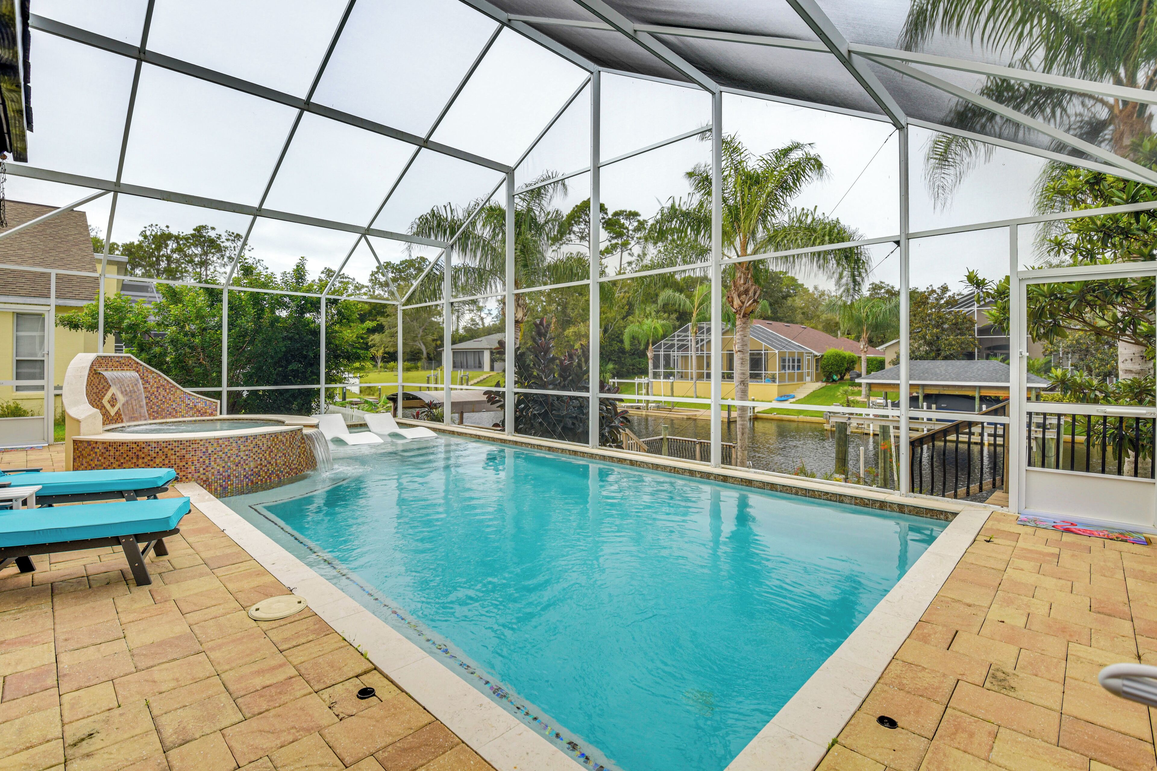 Une piscine intérieure protégée par une paroi de verre, entourée d’un patio aménagé avec des chaises longues et un jacuzzi.