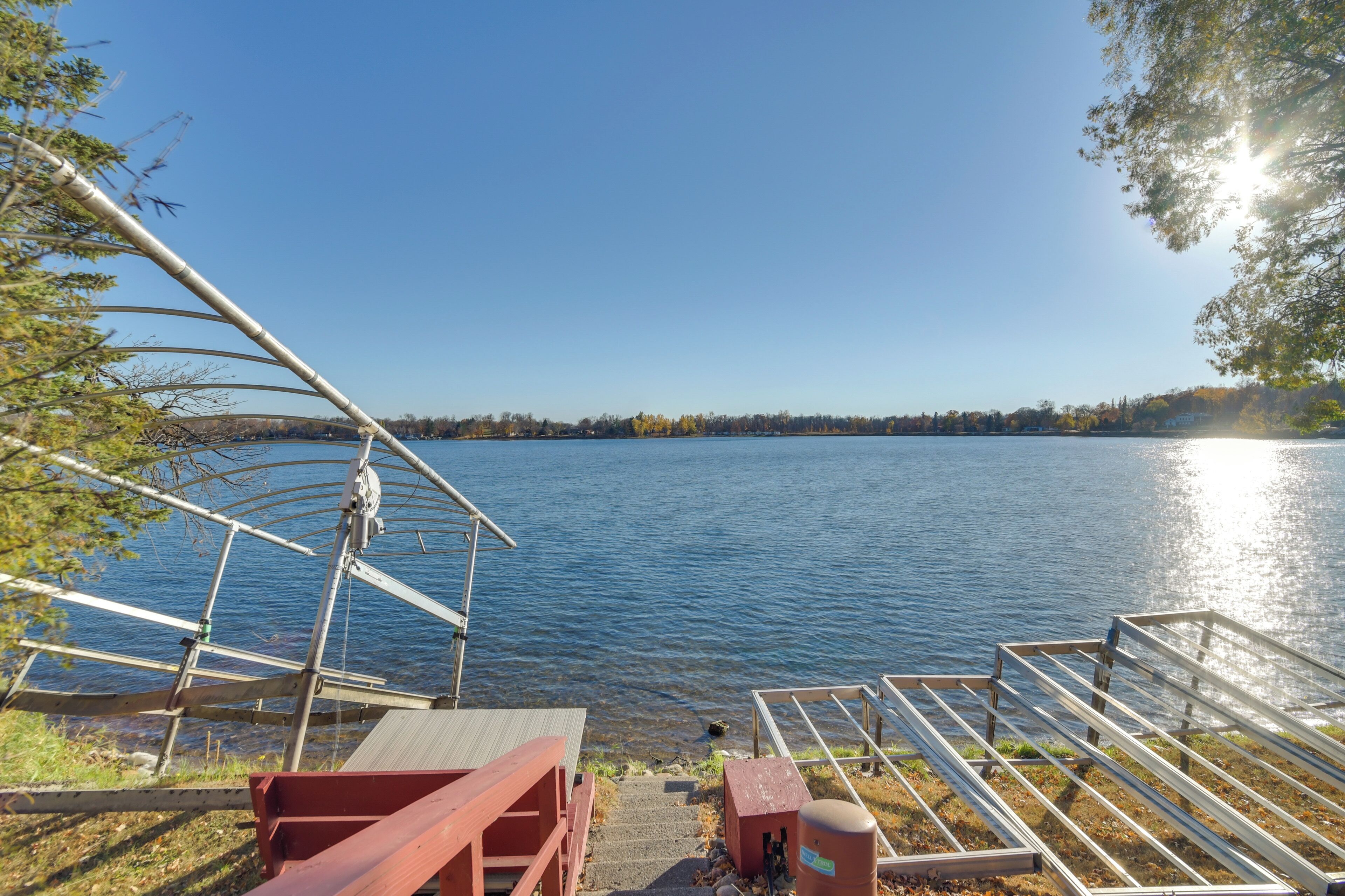 A lakeside dock with steps leading into the water, a metal railing, and a red bench.