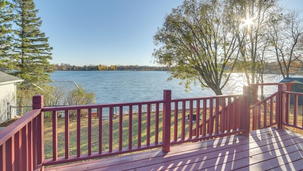 Une terrasse en bois avec une rambarde rouge donnant sur un lac.