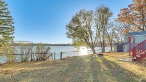 Une propriété située au bord d’un lac, dotée d’une cour clôturée, d’un escalier rouge et d’un petit abri de jardin.