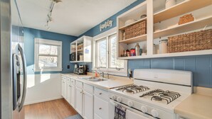Une cuisine avec des meubles blancs, une cuisinière, un évier et une fenêtre.