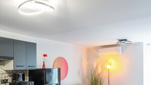 A modern kitchen with grey cabinets, a black refrigerator, and a microwave. There is a dining area with a round table and four chairs. The room has a grey sofa with colorful cushions, a small side table, and a tall floor lamp. - [Piazza Erbe] In city center up to 4 guests with parking (Verona)