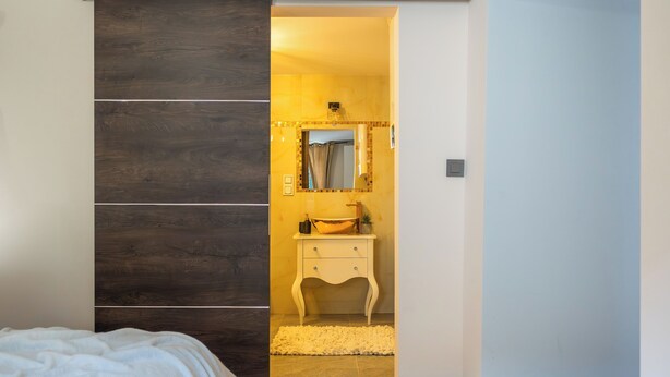A bedroom with a bed, a wooden wardrobe, a bathroom with a sink and mirror, and a white rug. - [Piazza Erbe] In city center up to 4 guests with parking (Verona)