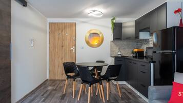 Une cuisine moderne avec des meubles de couleur sombre, une table de salle à manger ronde entourée de chaises noires et un coussin rouge sur un canapé gris.