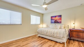 A bedroom with a bed, a ceiling fan, a nightstand, and a painting on the wall.