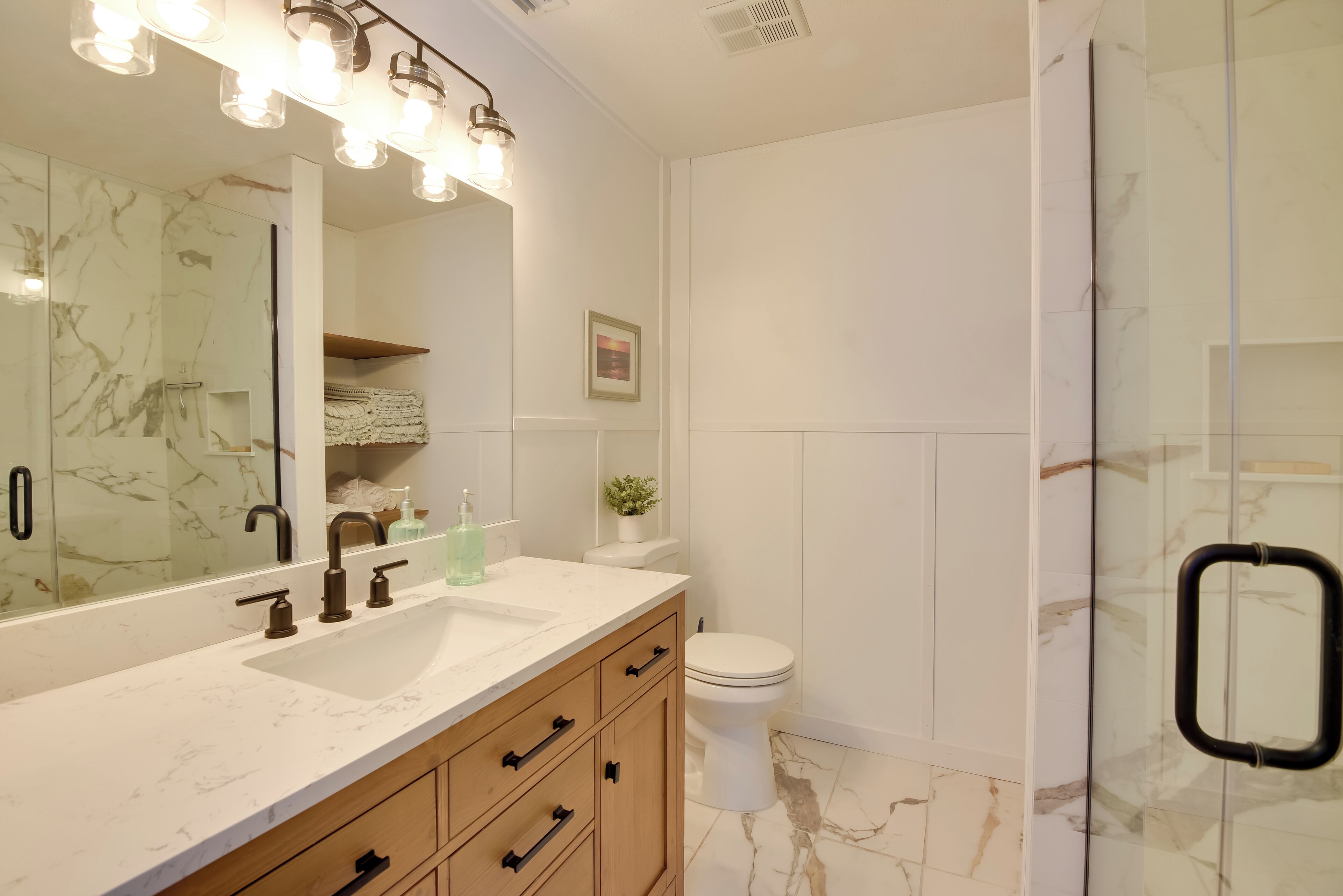A modern bathroom with a marble sink, a large mirror, and a glass shower enclosure.