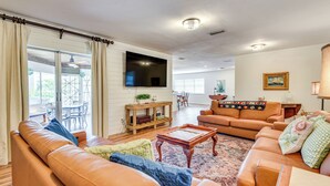 A living room with a sofa, a coffee table, and a television. There is a window with curtains and a view of the outdoors.
