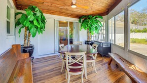 A dining area with a wooden ceiling, large windows, and potted plants.